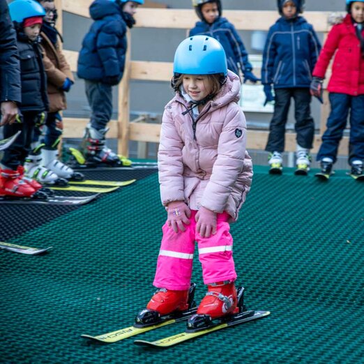 Kind fährt auf Skiern kleine Rampe auf Kunststoff-Piste hinunter | © Albert Reiter