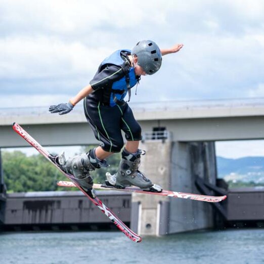 Kind springt auf Skiern über Sprungschanze ins Wasser | © Albert Reiter