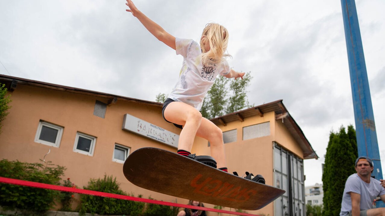Mädchen springt mit angeschnalltem Snowboard auf Slackline | © Albert Reiter