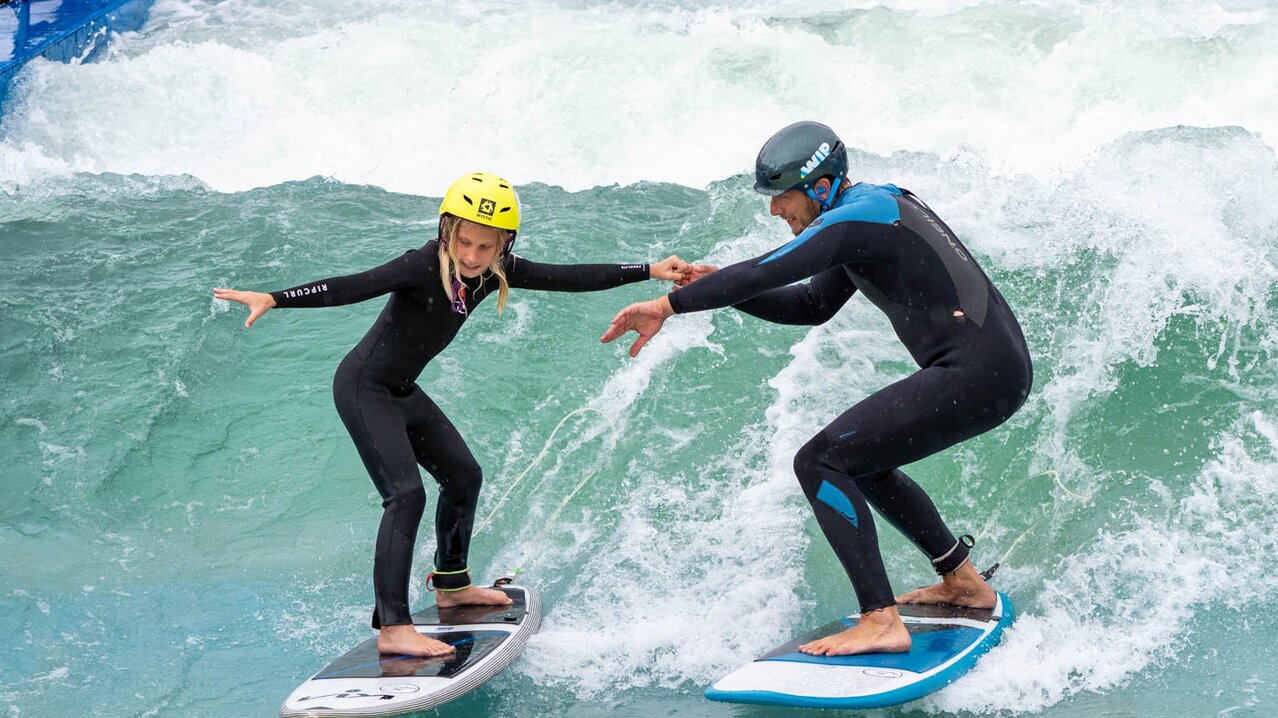 Mädchen und Trainer surfen auf zwei Surfbrettern auf Welle | © Albert Reiter