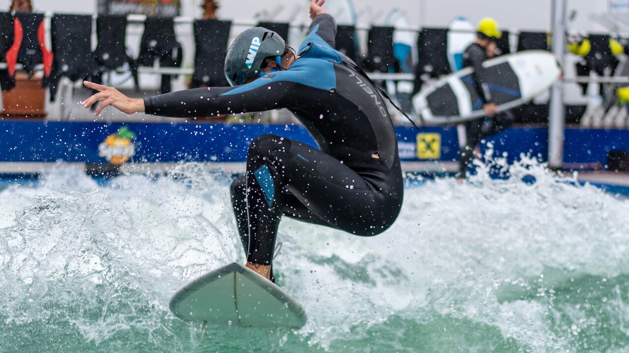 Mann springt mit Surfboard auf einer Welle | © Albert Reiter