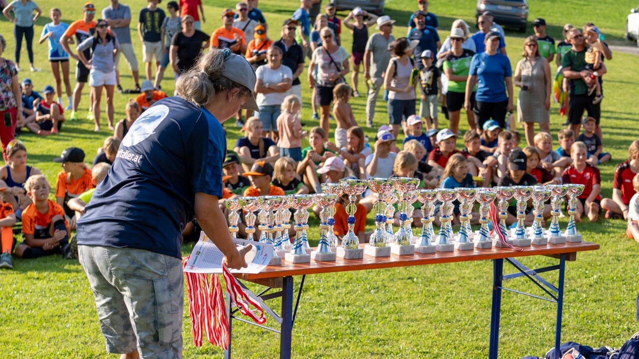 ein Tisch mit Pokalen, dahinter Kinder sitzend im Rasen | © Albert Reiter