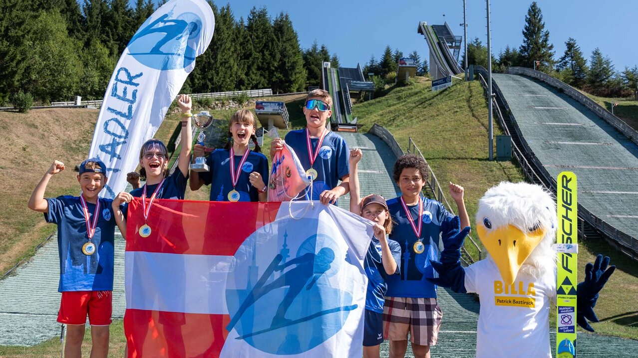 sechs Medaillengewinner:innen der Wiener Stadtadler stehen für Gruppenfoto auf Podium, Schanzenanlage im Hintergrund | © Albert Reiter