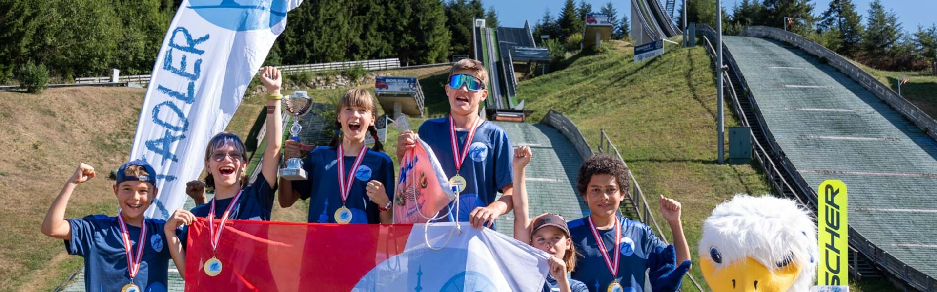 sechs Medaillengewinner:innen der Wiener Stadtadler stehen für Gruppenfoto auf Podium, Schanzenanlage im Hintergrund | © Albert Reiter