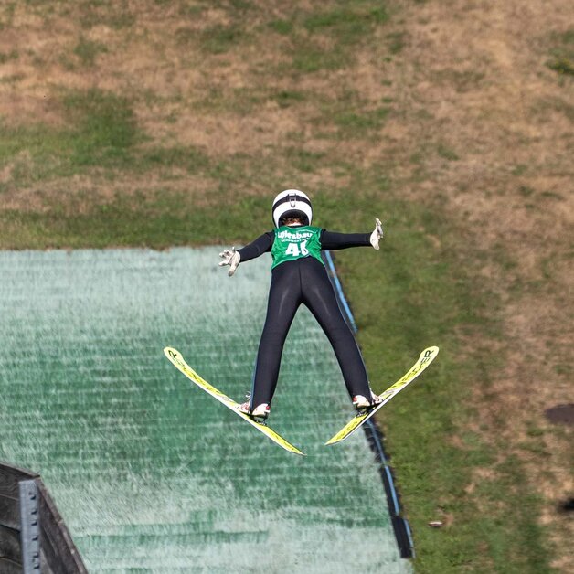 Skispringer in der Luft, Aufnahme von Hinten, im Hintergrund Auslaufzone | © Albert Reiter